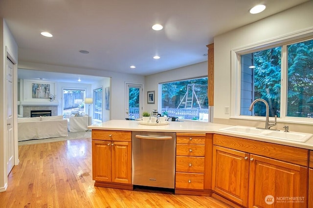 kitchen with stainless steel dishwasher, brown cabinetry, a sink, open floor plan, and light wood-style floors
