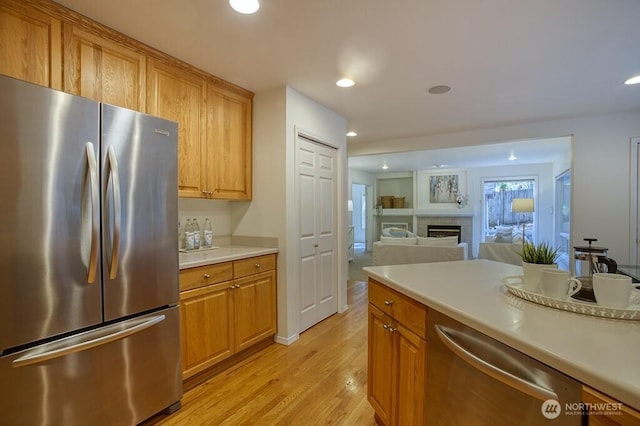 kitchen with appliances with stainless steel finishes, light wood-type flooring, light countertops, a fireplace, and recessed lighting