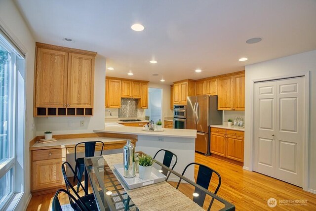 kitchen with appliances with stainless steel finishes, recessed lighting, light countertops, light wood-style flooring, and decorative backsplash