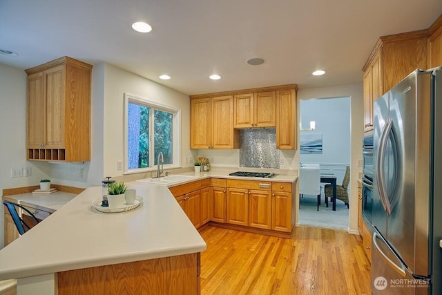 kitchen with stainless steel appliances, a sink, light wood-style flooring, a peninsula, and light countertops