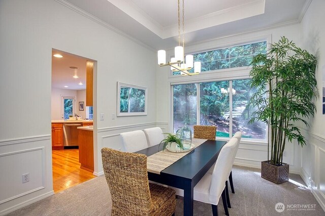 dining space with a chandelier, light colored carpet, a decorative wall, ornamental molding, and a wainscoted wall