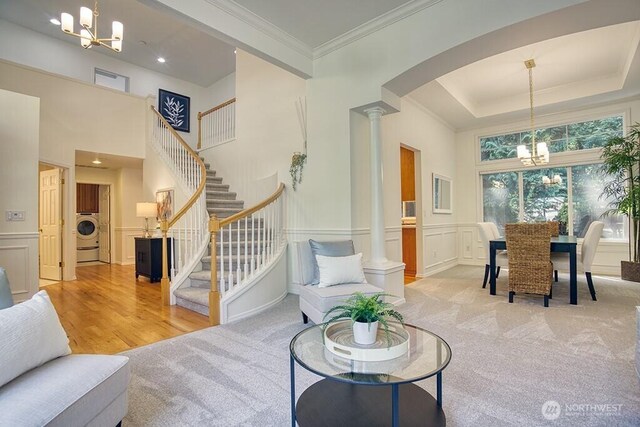 carpeted living room with ornate columns, a chandelier, washer / dryer, stairs, and a decorative wall