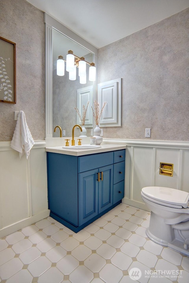 bathroom featuring a decorative wall, toilet, vanity, a wainscoted wall, and tile patterned floors