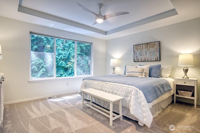 carpeted bedroom with a tray ceiling, baseboards, and ceiling fan