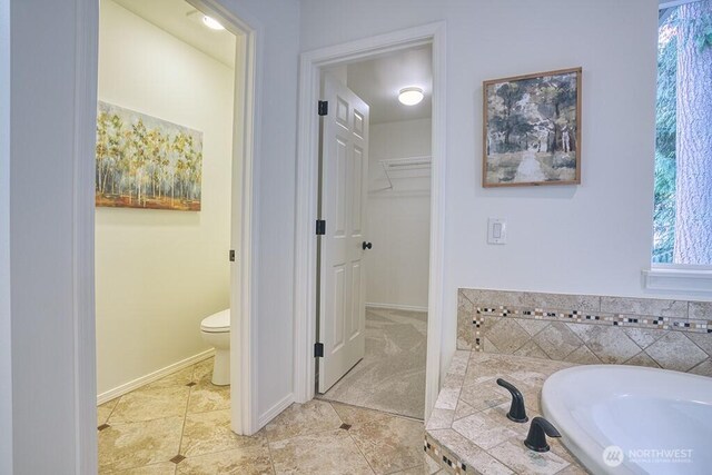 full bathroom featuring a bath, tile patterned floors, toilet, baseboards, and a spacious closet