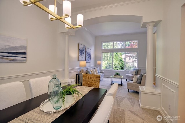 dining space with ornate columns, crown molding, a decorative wall, light colored carpet, and wainscoting