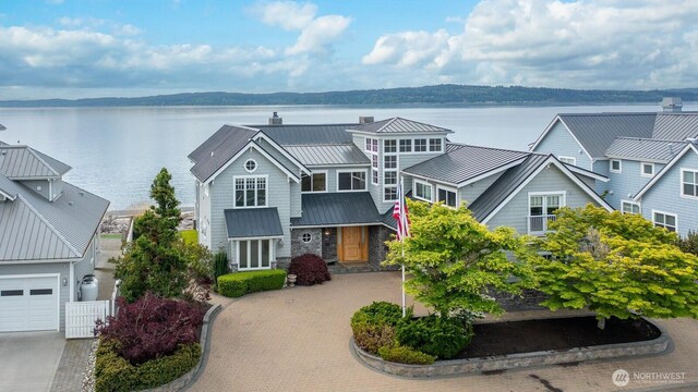 view of front facade with a standing seam roof, a chimney, decorative driveway, metal roof, and a water view