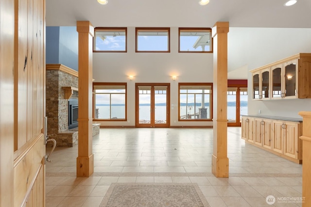 unfurnished living room with decorative columns, light tile patterned flooring, a stone fireplace, a towering ceiling, and recessed lighting