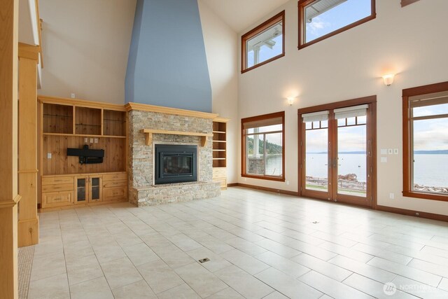 unfurnished living room with a high ceiling, healthy amount of natural light, a stone fireplace, tile patterned flooring, and baseboards