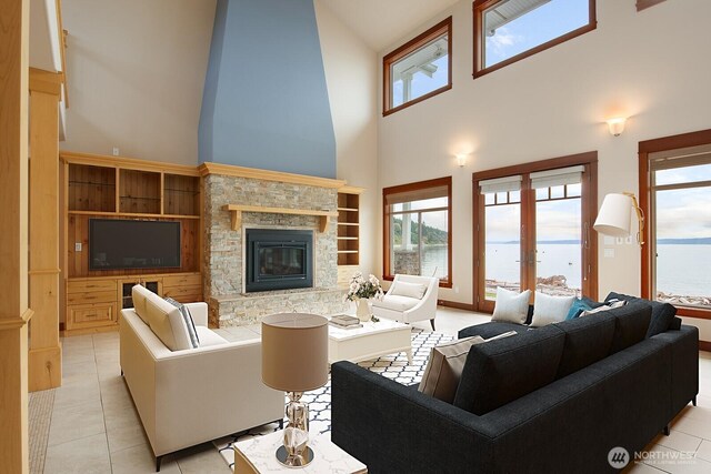 living area featuring healthy amount of natural light, a high ceiling, light tile patterned floors, and a stone fireplace