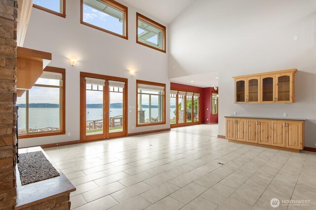 unfurnished living room with a high ceiling, a water view, and baseboards