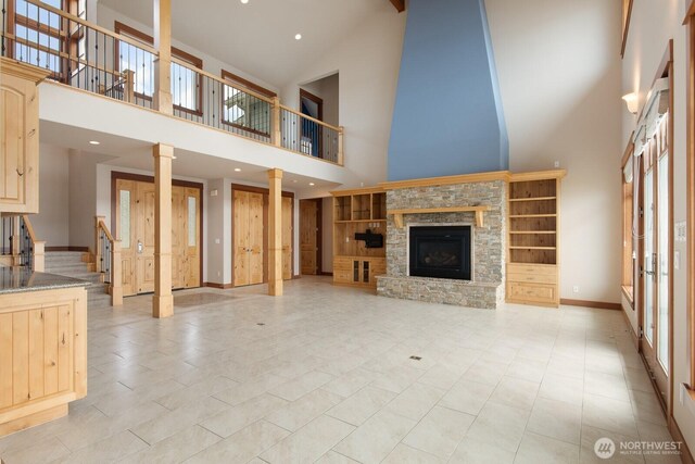 unfurnished living room with high vaulted ceiling, stairs, a stone fireplace, baseboards, and plenty of natural light