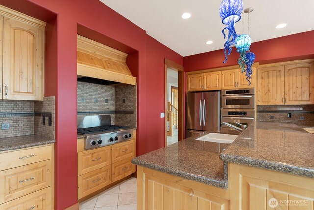 kitchen featuring appliances with stainless steel finishes, premium range hood, tasteful backsplash, a sink, and dark stone counters