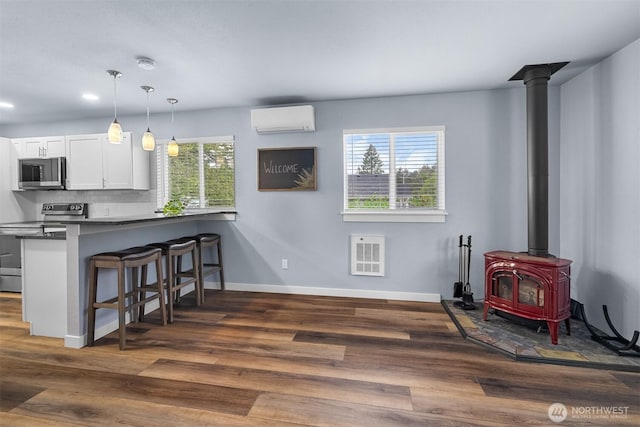 473 Mt Olympus Ave SE, Ocean Shores, WA 98569 - kitchen featuring appliances with stainless steel finishes, a wall mounted AC, a wood stove, a kitchen breakfast bar, and white cabinetry