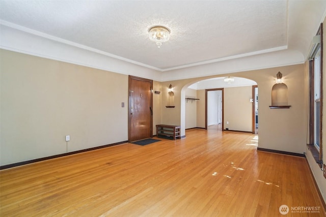 unfurnished room with arched walkways, light wood-style floors, and baseboards