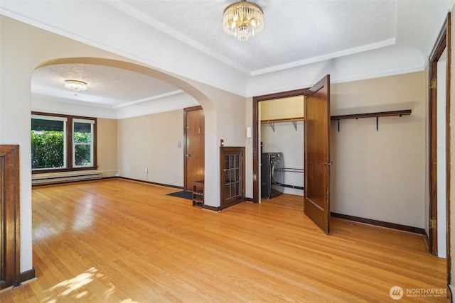 unfurnished bedroom with baseboard heating, arched walkways, light wood-style flooring, a chandelier, and baseboards
