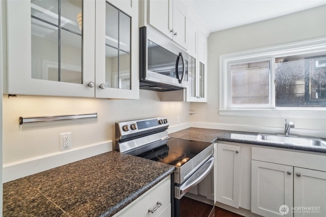 kitchen featuring appliances with stainless steel finishes, a sink, glass insert cabinets, and white cabinets
