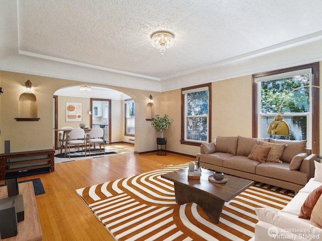 living room featuring arched walkways, a textured ceiling, light wood-type flooring, and baseboards