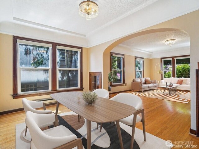 dining area featuring arched walkways, a chandelier, light wood-style floors, a textured ceiling, and a tray ceiling