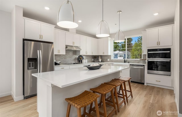 kitchen with under cabinet range hood, a sink, white cabinetry, backsplash, and appliances with stainless steel finishes