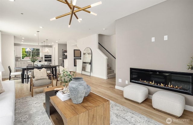 living room with stairs, recessed lighting, light wood-style flooring, baseboards, and a glass covered fireplace