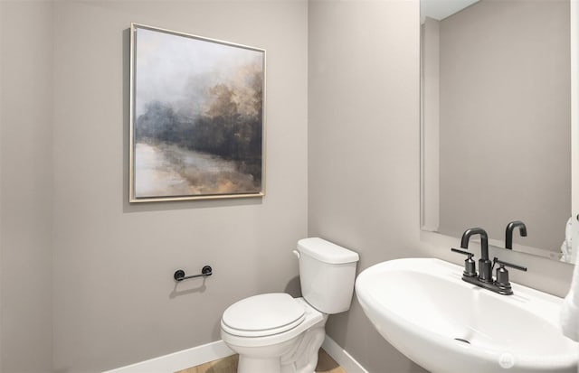 half bathroom with toilet, baseboards, and a sink