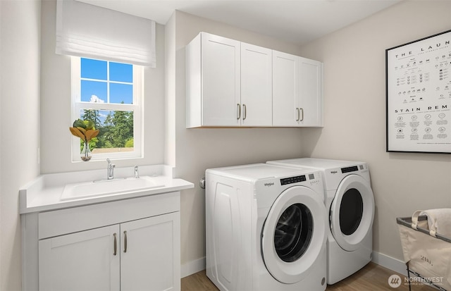 washroom with a sink, cabinet space, separate washer and dryer, baseboards, and light wood-style floors