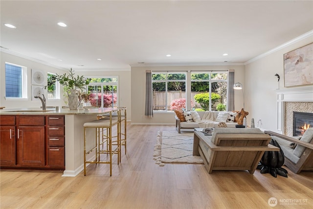 living room featuring light wood-style floors, a tile fireplace, ornamental molding, recessed lighting, and baseboards