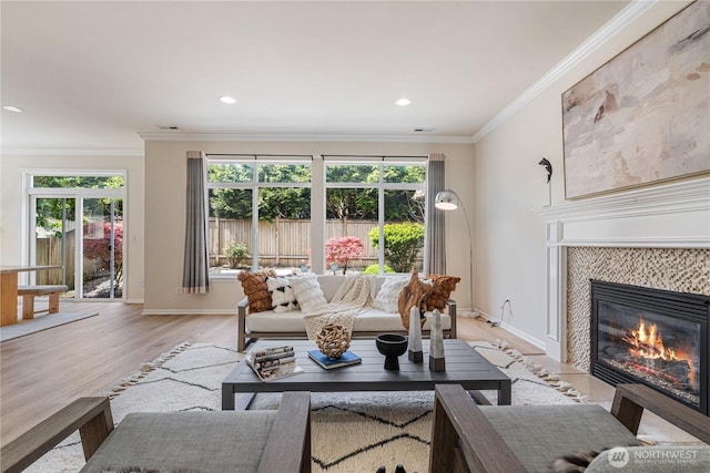 living room with plenty of natural light, a tile fireplace, light wood-style flooring, crown molding, and baseboards