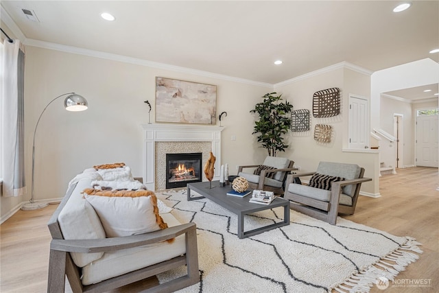 living room with light wood-style flooring, ornamental molding, a glass covered fireplace, recessed lighting, and baseboards