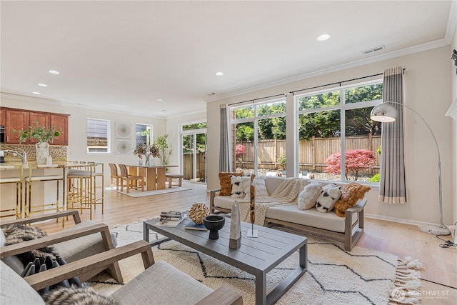 living area featuring light wood-style flooring, ornamental molding, recessed lighting, and baseboards