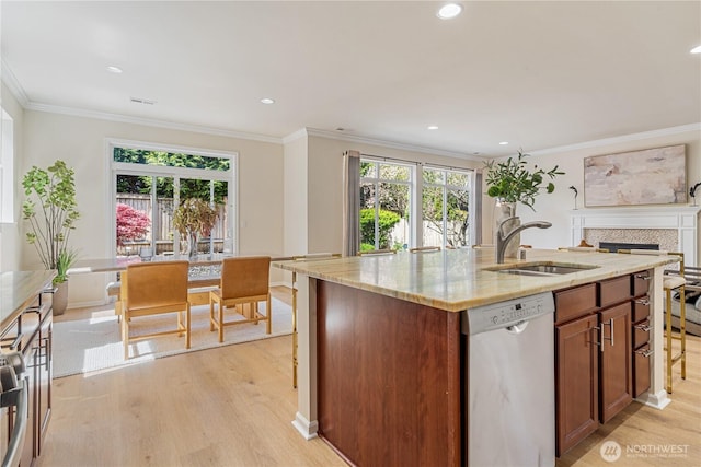 kitchen with stainless steel dishwasher, a sink, light wood-style flooring, light stone countertops, and a center island with sink
