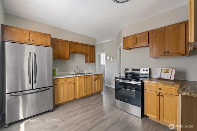 kitchen featuring appliances with stainless steel finishes, a sink, light wood-style floors, light countertops, and brown cabinetry
