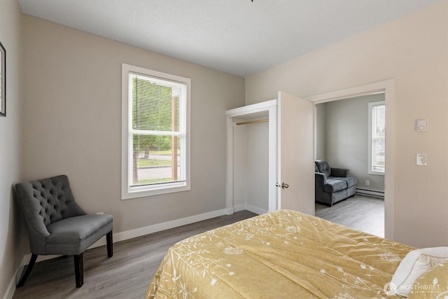 bedroom with a baseboard radiator, wood finished floors, and baseboards