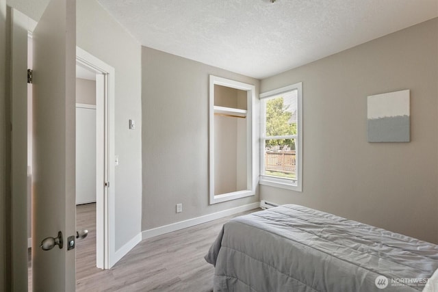 bedroom featuring wood finished floors, baseboards, a textured ceiling, and a baseboard heating unit