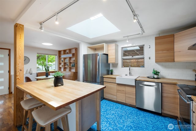 kitchen featuring track lighting, butcher block counters, stainless steel appliances, a sink, and a skylight