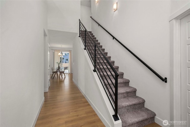 staircase featuring wood finished floors, baseboards, and a chandelier