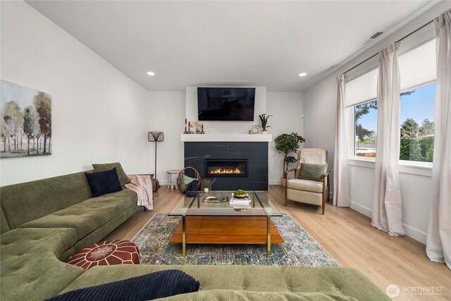 living area featuring wood finished floors, a glass covered fireplace, recessed lighting, and baseboards