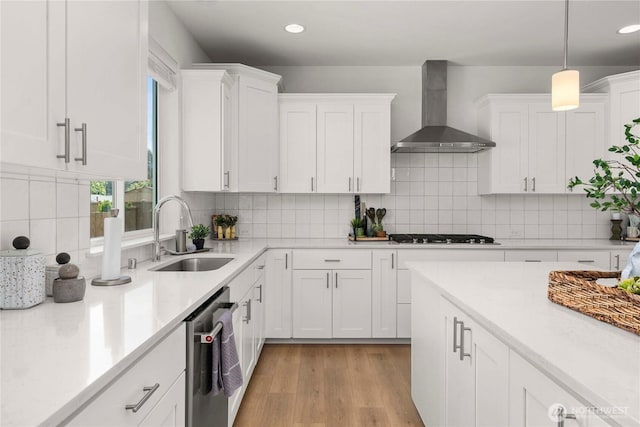 kitchen with wall chimney range hood, a sink, gas cooktop, dishwasher, and light countertops