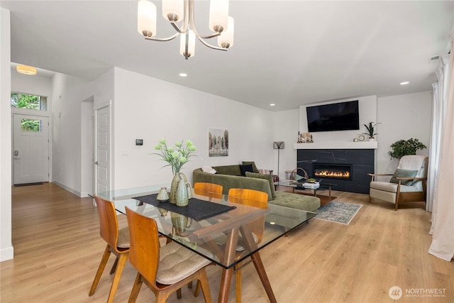 dining area with light wood-type flooring, a chandelier, a tile fireplace, baseboards, and recessed lighting