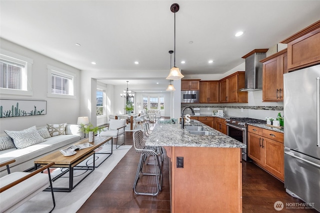 kitchen featuring light stone countertops, a sink, a kitchen bar, wall chimney exhaust hood, and stainless steel appliances