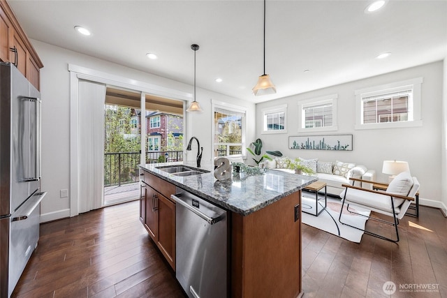 kitchen with a sink, dark stone counters, pendant lighting, dark wood finished floors, and appliances with stainless steel finishes