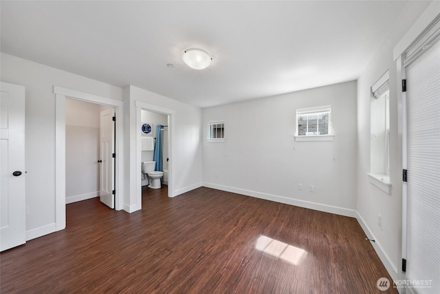 unfurnished bedroom with a closet, wood finished floors, baseboards, and a spacious closet