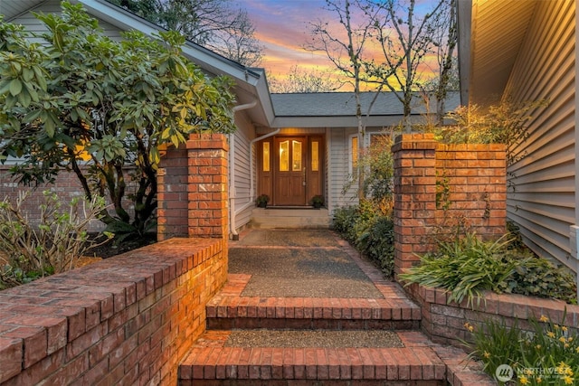 exterior entry at dusk featuring roof with shingles