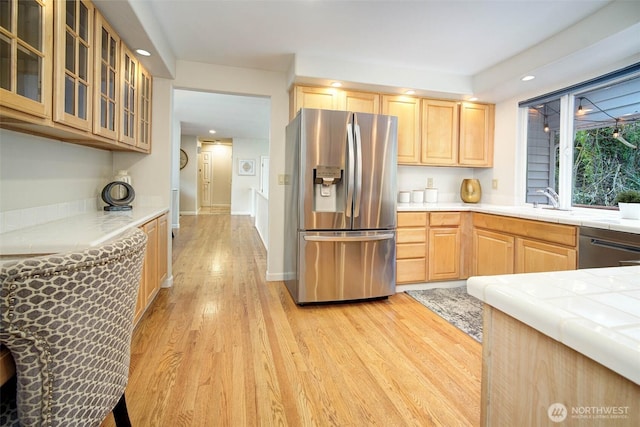 kitchen featuring light brown cabinets, tile countertops, light wood-style flooring, glass insert cabinets, and appliances with stainless steel finishes
