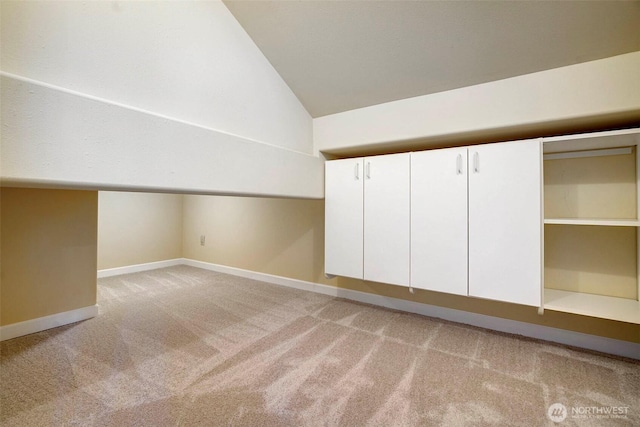 additional living space featuring light colored carpet, lofted ceiling, and baseboards