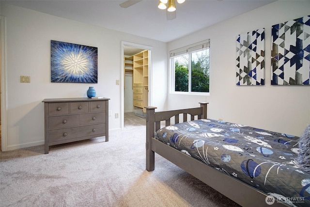 carpeted bedroom with ceiling fan, a spacious closet, and baseboards