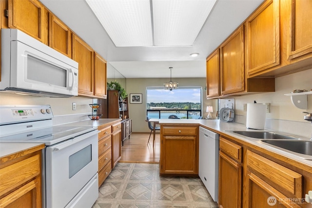 kitchen with white appliances, light countertops, brown cabinetry, a peninsula, and a sink