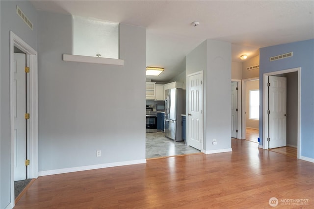 unfurnished living room featuring light wood finished floors, lofted ceiling, and baseboards