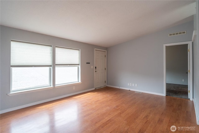 spare room with light wood finished floors, baseboards, and lofted ceiling